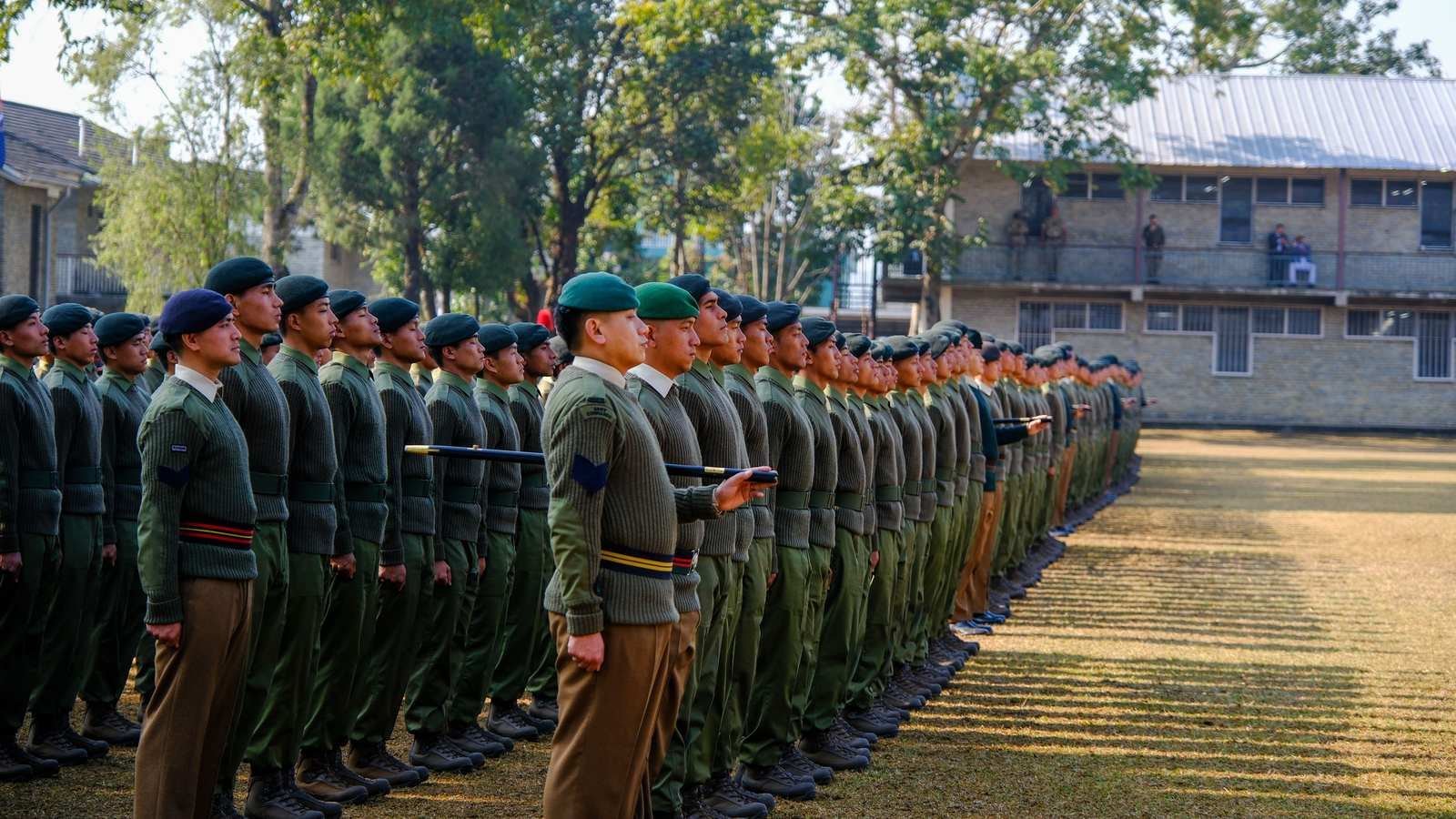 Cadets in green berets standing in formation in front of a school building