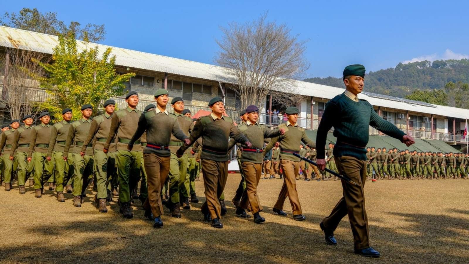 Cadets in uniform marching past a school building